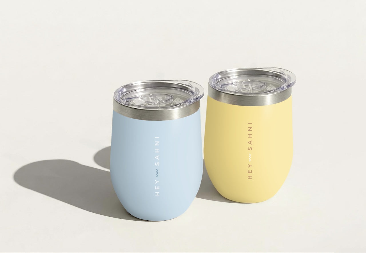 Two insulated HEY SAHNI Cups, one blue and one yellow, on a light background.