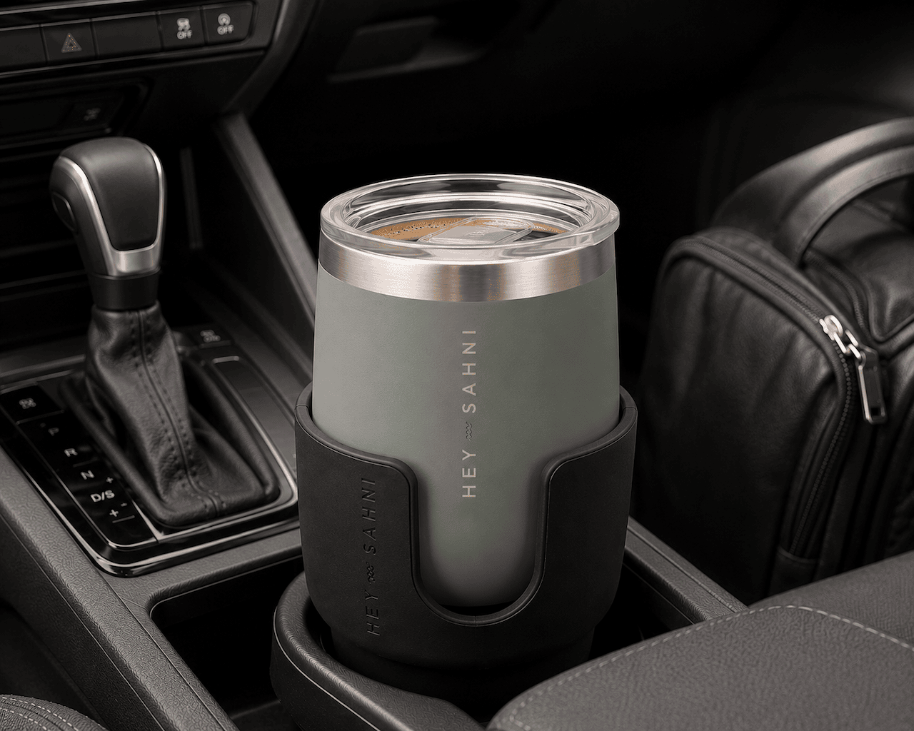 Pine HEY SAHNI insulated tumbler with a black sleeve in a car cup holder, featuring 'Hey Sahni' branding.