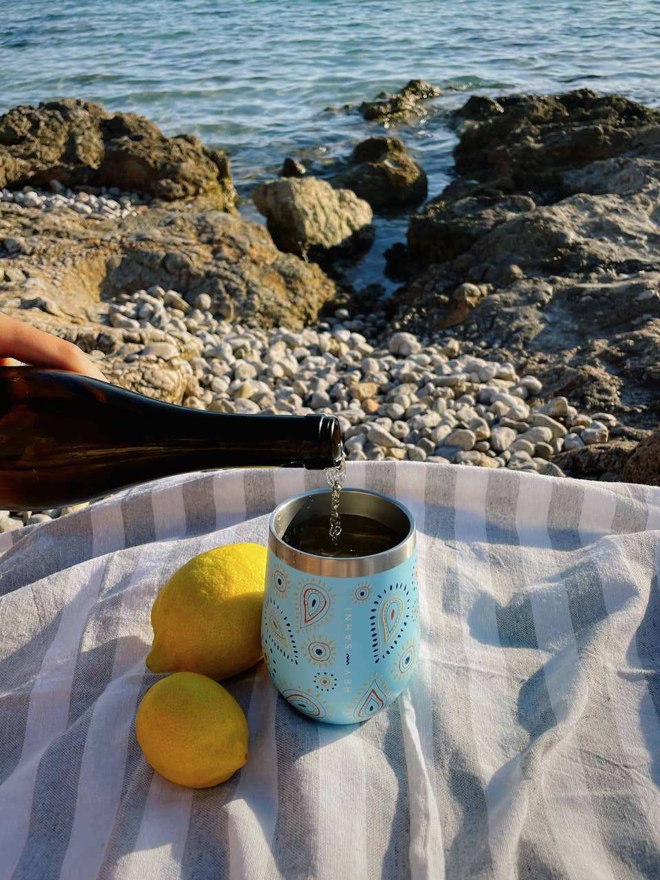Eco-friendly stainless steel cup "La Isla" keeping drinks hot or cold, featuring a sliding lid, with a beach backdrop.