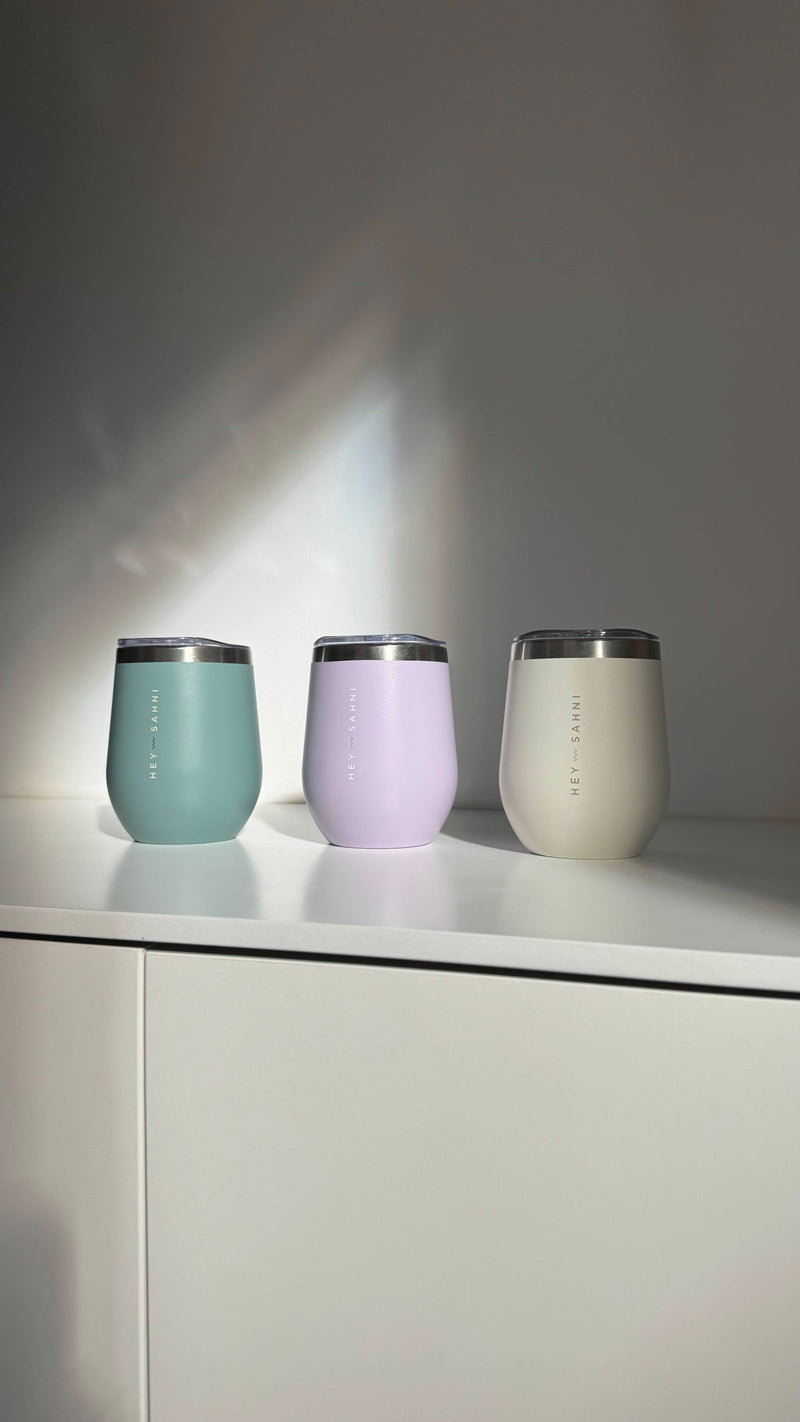 Three HEY SAHNI stainless steel cups in mint, lilac and cream in morning sunlight