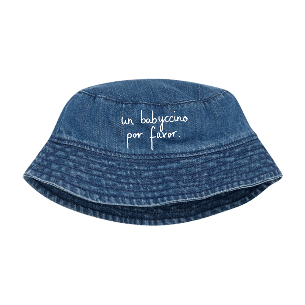 A blue HEY SAHNI denim bucket hat with white cursive text reading 'un babuccino por favor.' on the front, shown against a solid green background.
