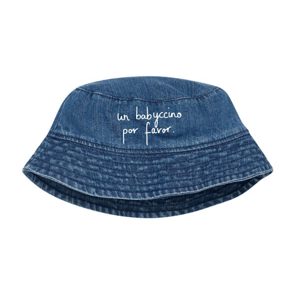 A blue HEY SAHNI denim bucket hat with white cursive text reading 'un babuccino por favor.' on the front, shown against a solid green background.