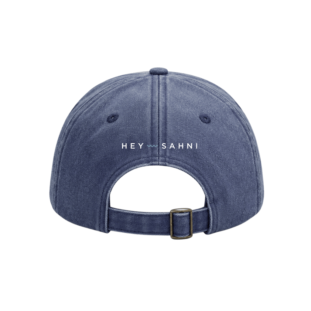 A blue denim baseball cap shown from the back, featuring the text 'HEY SAHNI' printed in white across the center, set against a solid green background.