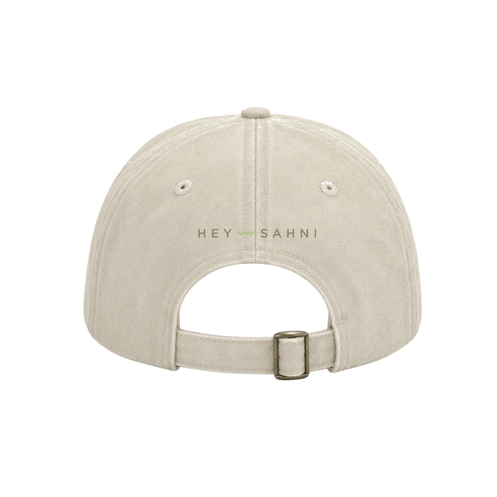 Back view of a light beige baseball cap with 'HEY SAHNI' embroidered on the center back, shown against a solid green background.