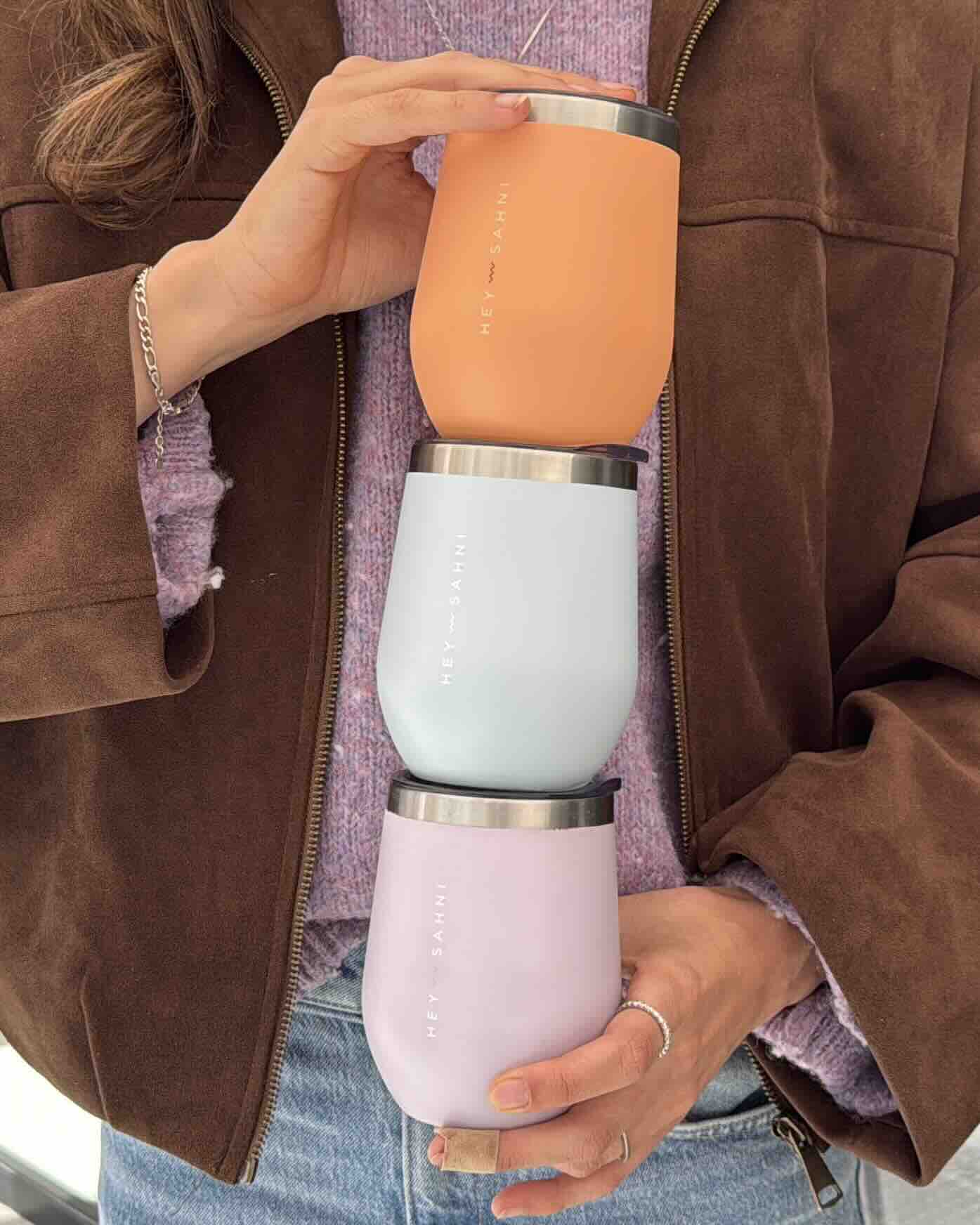 Stacked reusable coffee cups in spring colors, held casually by Lisa