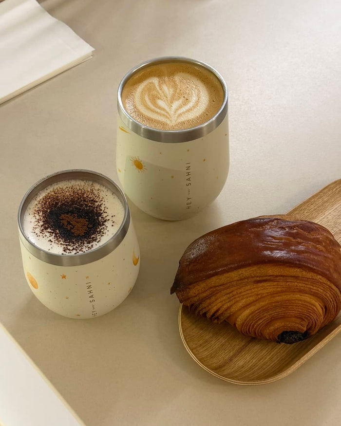 Zwei HEY SAHNI Becher mit Latte Art und Croissant